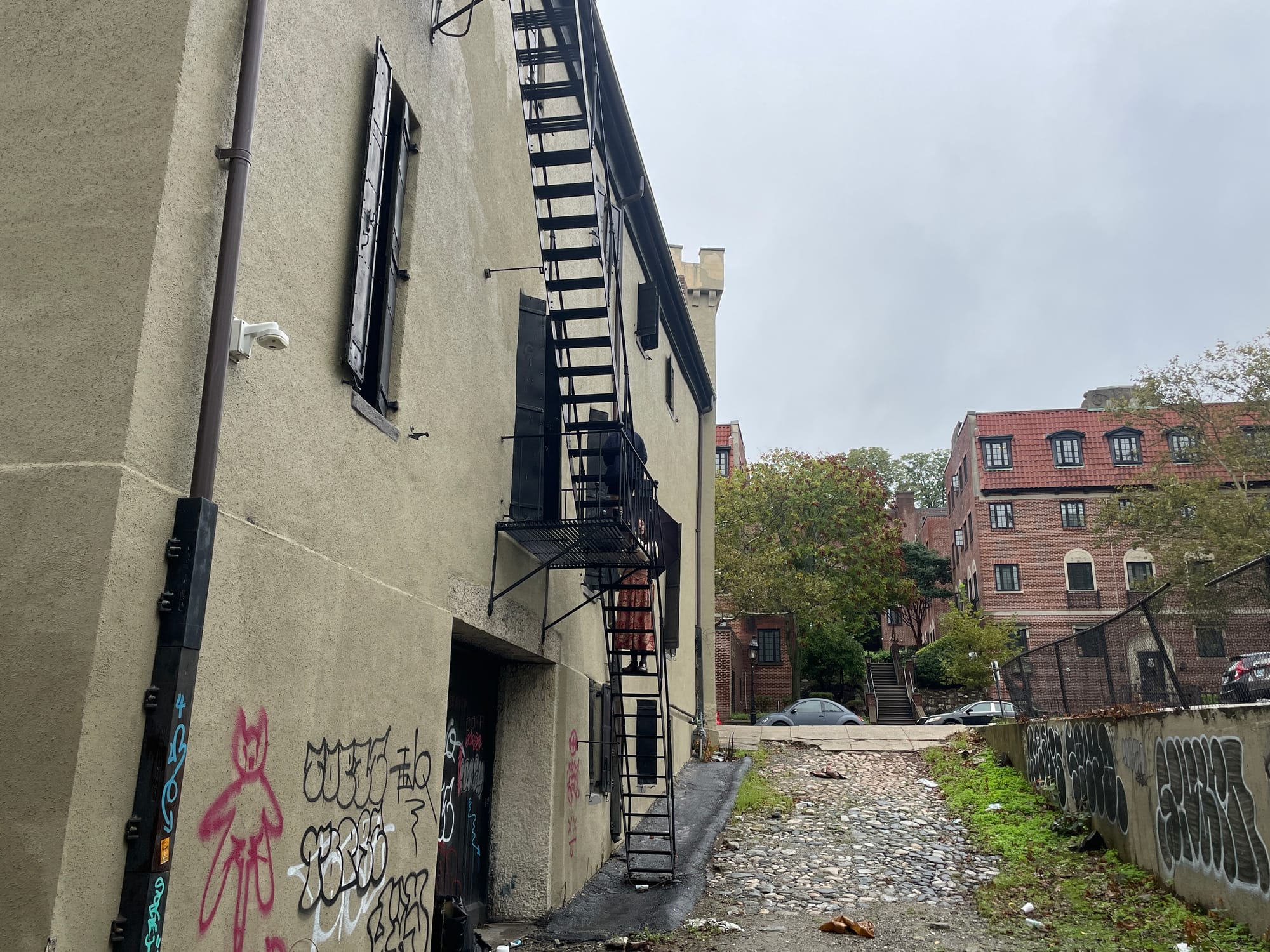 A graffiti building wall with a black fire escape over a rubble alley lane