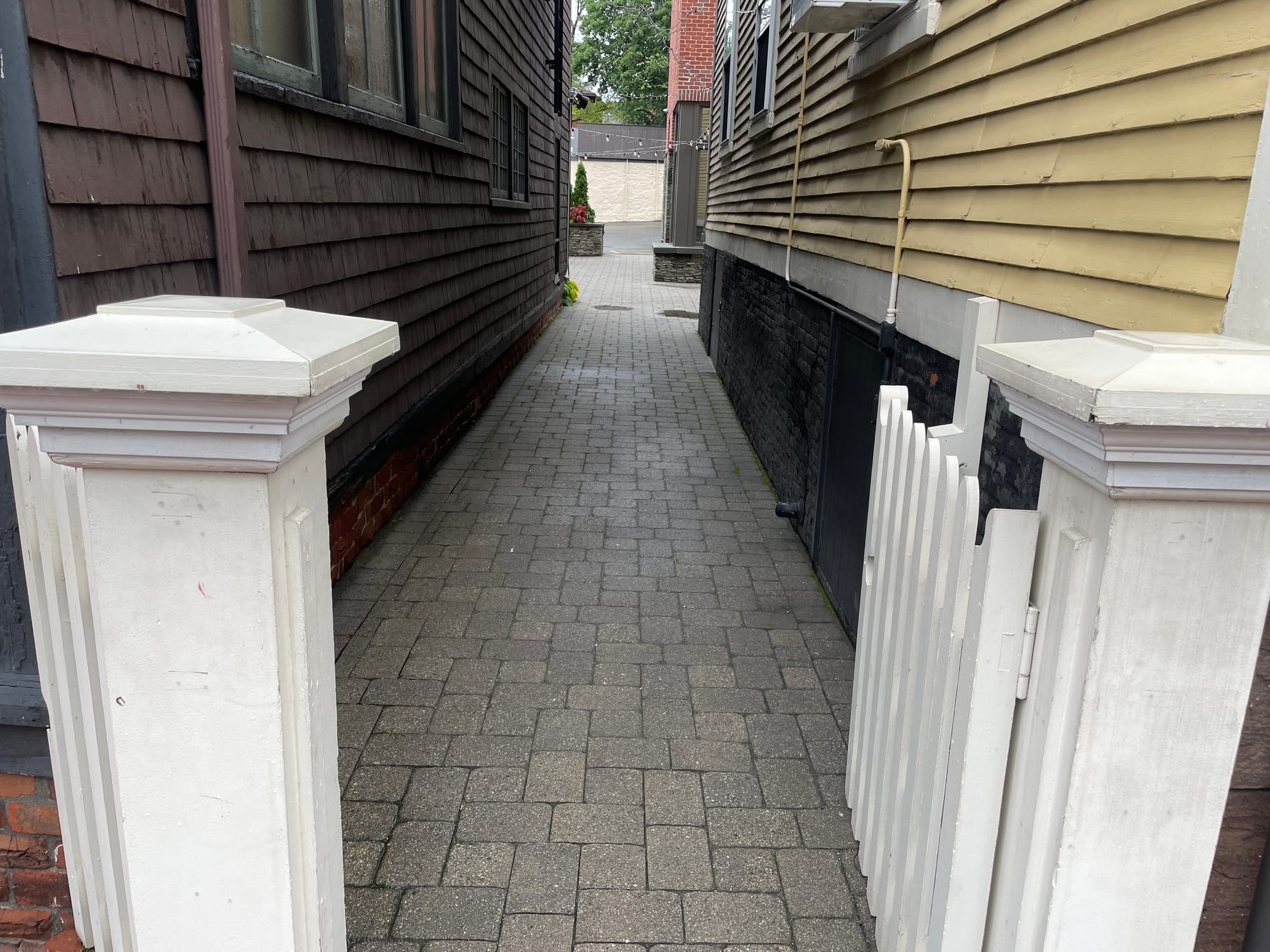 A narrow cobblestone passage between a dark-shingled house and a yellow clapboard house