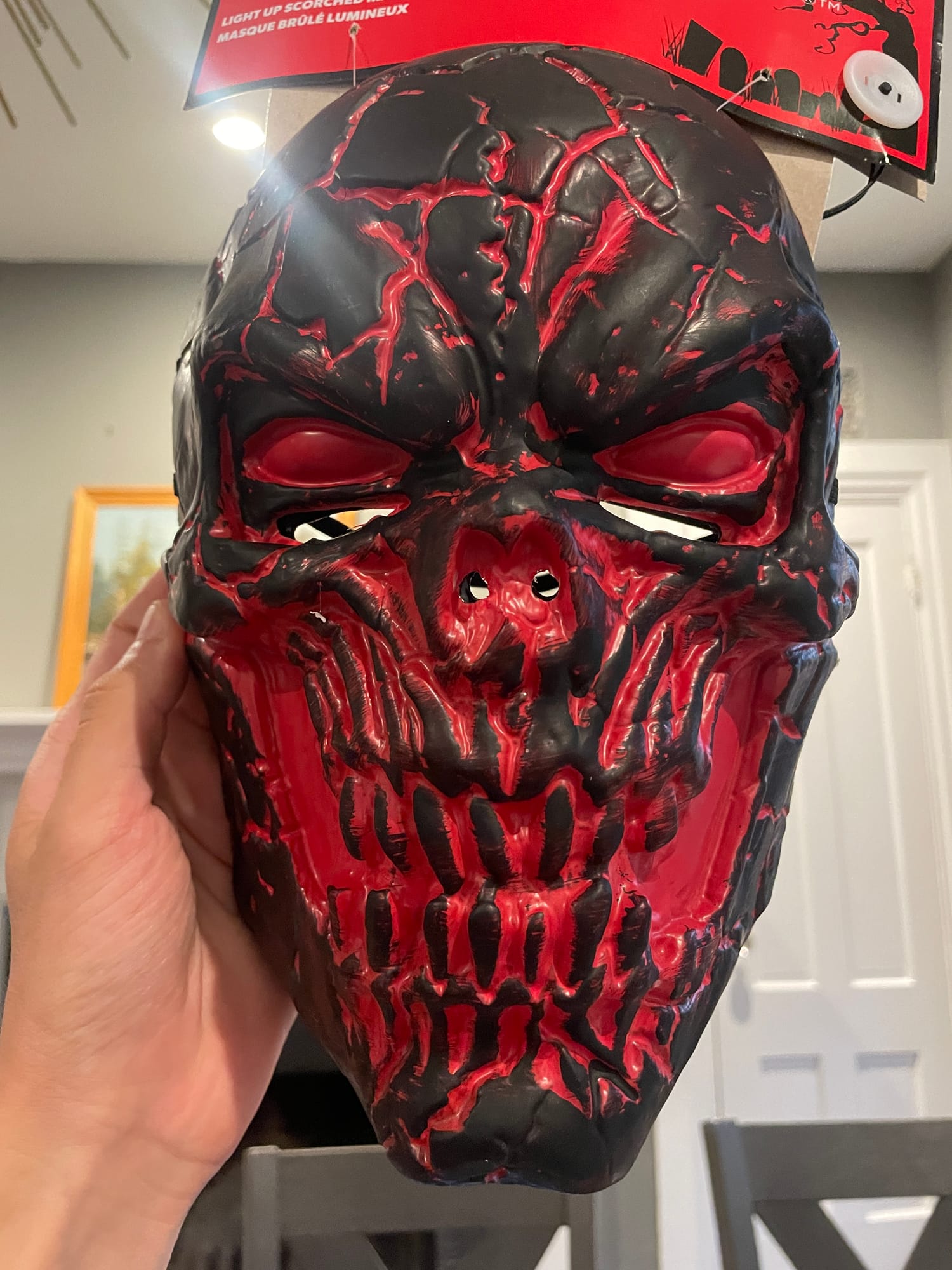 A red-and-black demon mask held in hand, still on its Savers retail packaging